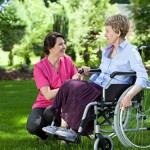 Happy senior woman on wheelchair with caring caregiver outdoors